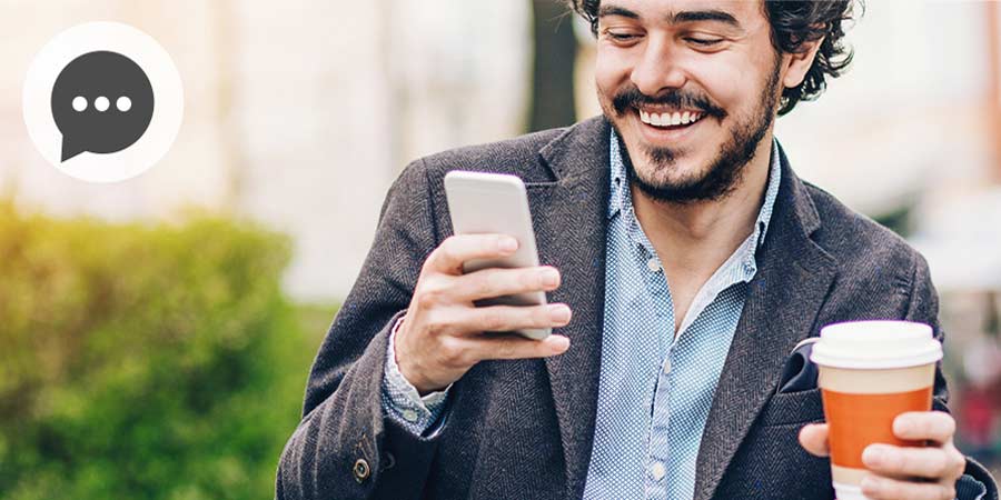 Handsome man reading a message on his mobile device while drinking a coffee