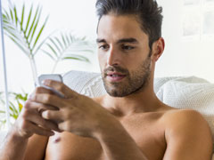 Sexy man met ontbloot bovenlijf die een mobiel gebruikt om te chatten op Messenger.