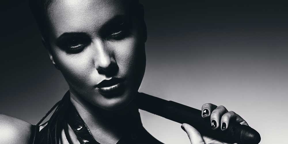 Sexy woman with black hair in the BDSM scene holding a leather flogger