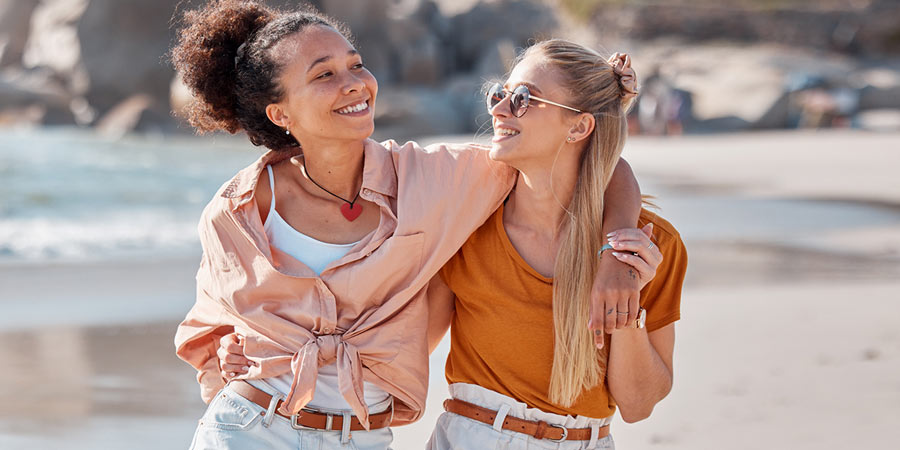 Two attractive female best friends walking down the beach and smiling 