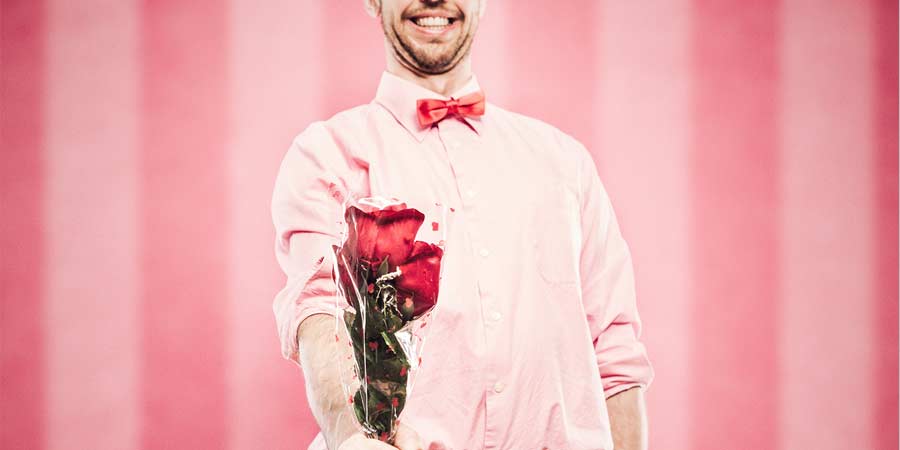 Geeky man in a pink shirt and bowtie holding a bunch of red roses