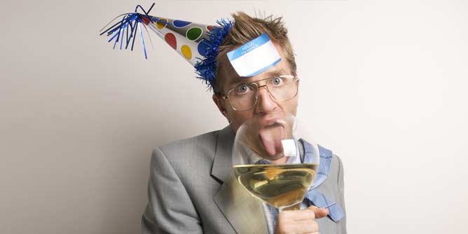 Drunk man wearing a party hat and drinking out of a huge glass of white wine at an office party