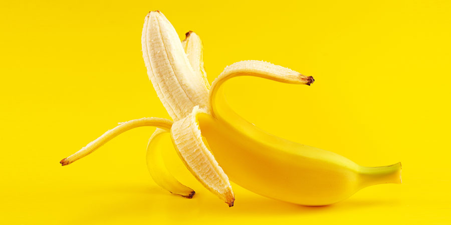 Ripe banana which is being unpeeled to represent an uncut cock