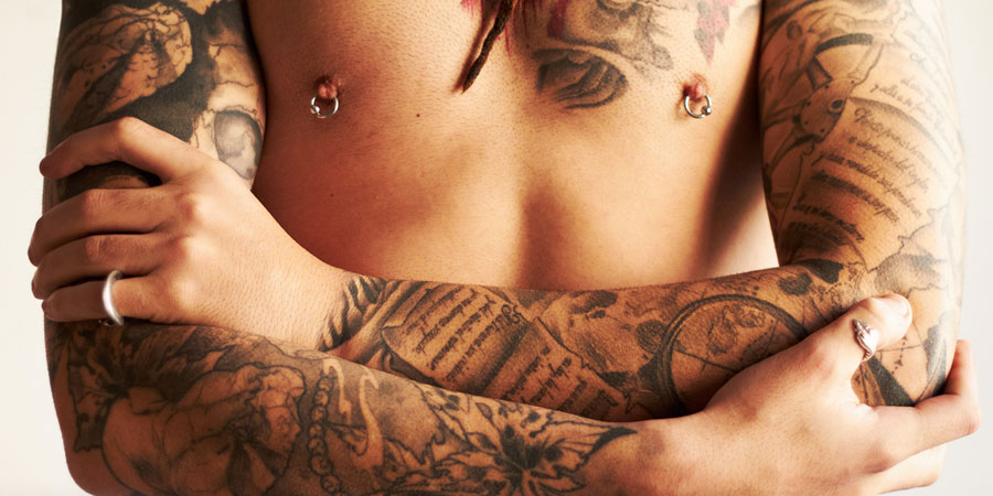 Man's torso with heavily tattoed arms and pierced nipples