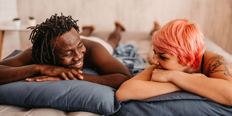 Interracial couple lying on a bed asking each other questions
