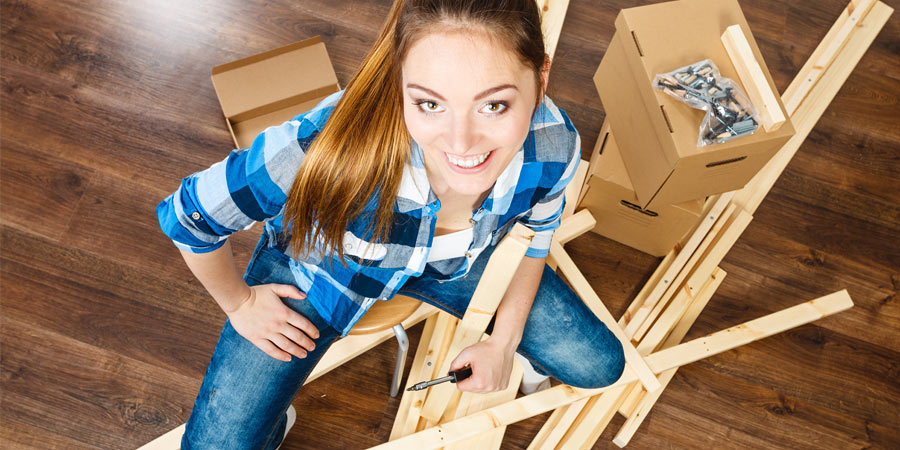 Attractive woman wearing a check shirt smiling as she assembles a flat pack 