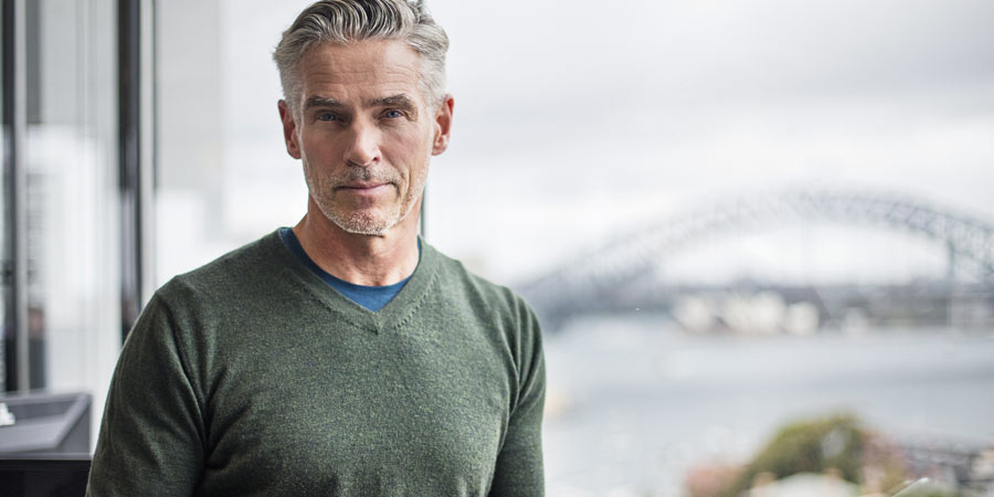 Attractive mature man with grey hair in an office with the Sydney Harbour bridge in the background