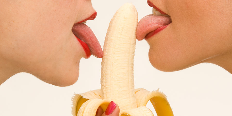 Two women licking either side of a banana 