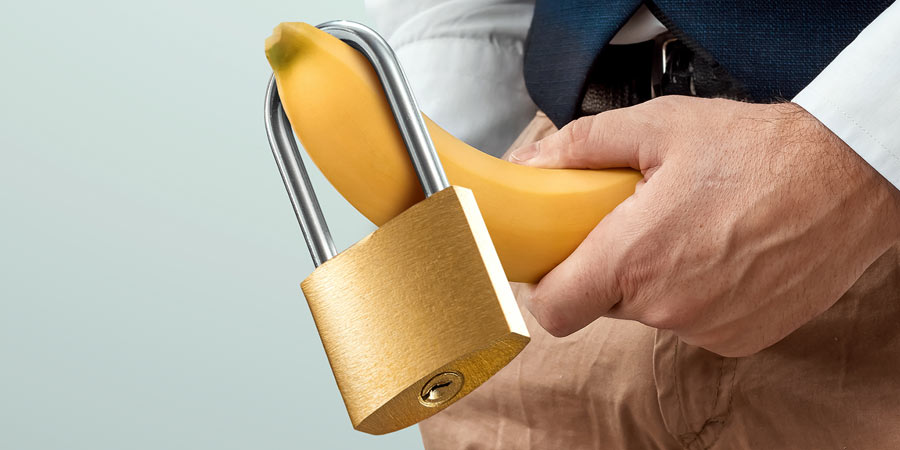 Man holding a plastic banana with a lock hanging from it in front of his groin as though it was his penis