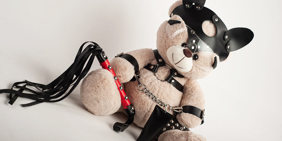 Teddy bear dressed in fetish leather gear and holding a flogger