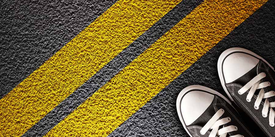 Feet in black and white sneakers hesitant to cross a double yellow line boundary painted on a road