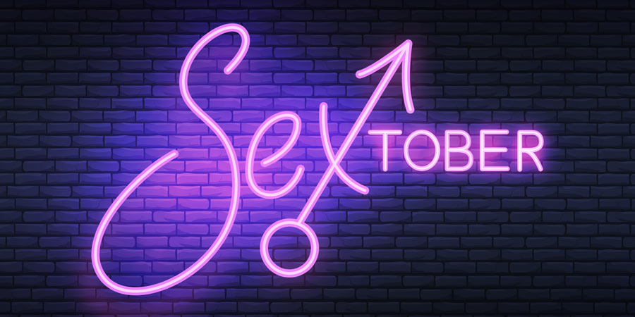 Neon sign of the word Sextober in purple which incorporates the male gender symbol as the X illuminating a brick wall 
