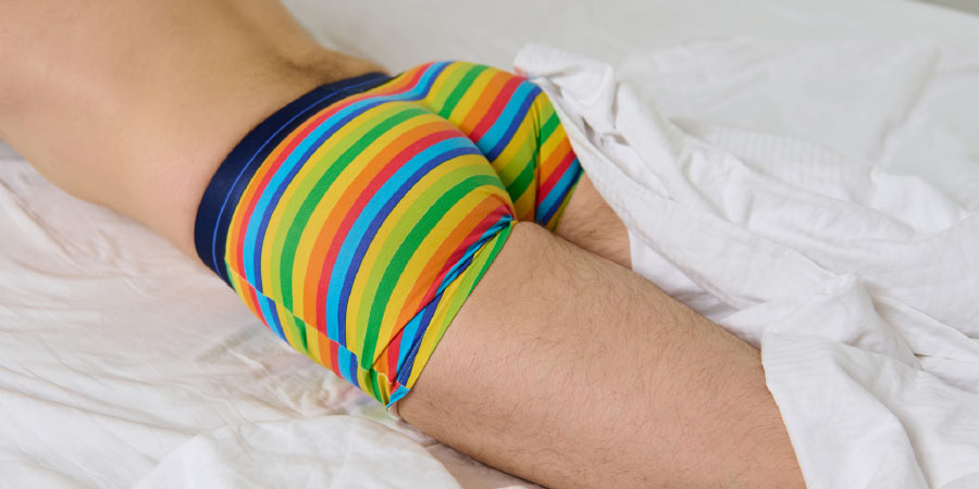 Man lying facedown on a bed wearing brightly striped boxer briefs