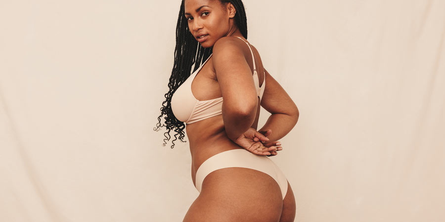 Very attractive dark skinned woman in skin coloured underwear turning to look at the camera and showing off her curves