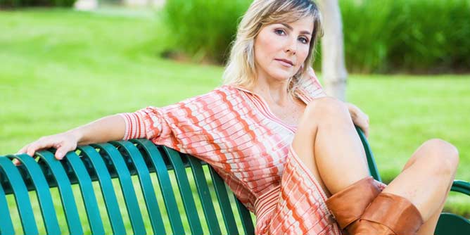 Attractive blonde mature woman with a short skirt and boots sitting on a park bench