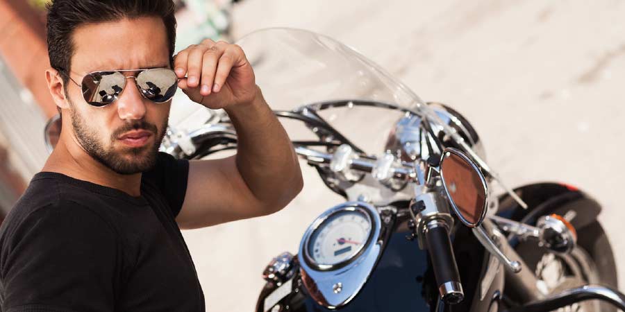 Charismatic man wearing aviator sunglasses and a black tshirt sitting on his motorbike